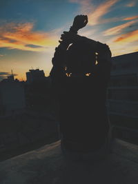 Silhouette woman in city against sky during sunset