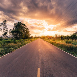 Road by trees on field against sky at sunset