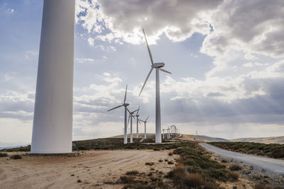 Wind turbines lined up by clouds in sky