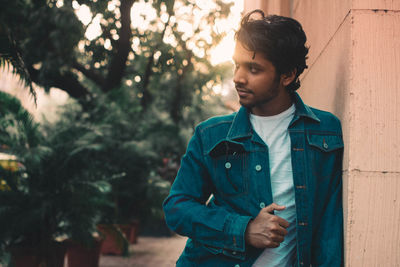 Young man looking away while leaning on wall