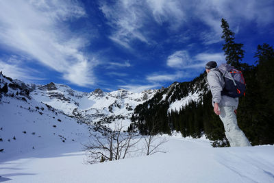 Rear view of man standing on snow covered mountains against sky