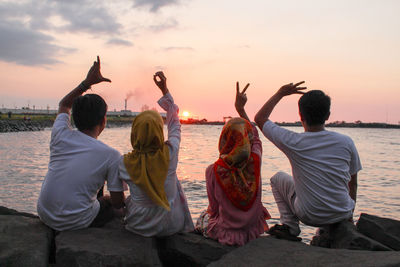 Rear view of friends gesturing love text at beach against sky