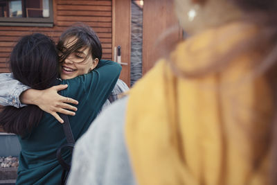 Happy female friends embracing each other outside house