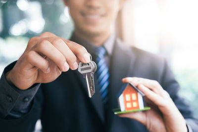 Midsection of businessman holding house keys and model home in office