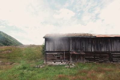 Old barn on field against cloudy sky