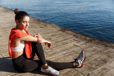 Full length of young woman sitting on shore