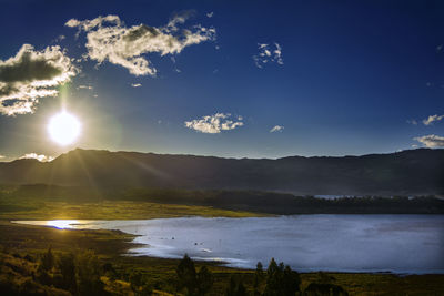 Scenic view of lake and mountains against bright sun