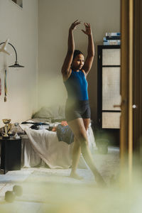 Dedicated teenage girl with hands raised exercising in bedroom at home