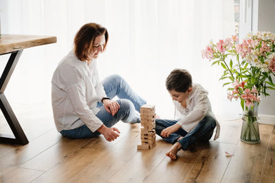 Mother with child son are sitting on the floor playing a board game of physical skill tower