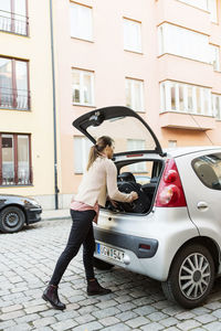 Side view of businesswoman loading luggage in car trunk on street