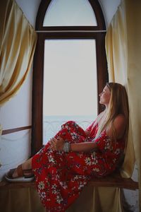 Side view of thoughtful woman looking through window at home