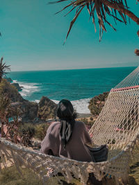 Rear view of woman sitting on hammock against sea