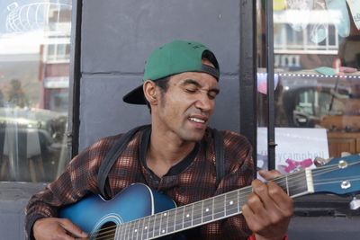 Young man playing guitar against building in city