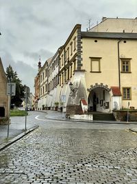 Wet street by buildings against sky in city