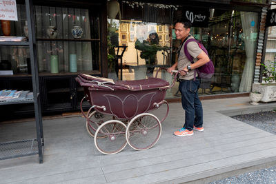 Side view of man holding old-fashioned baby stroller while standing outside store