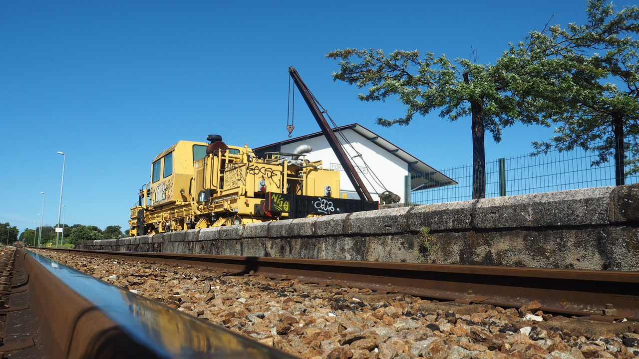 railroad track, rail transportation, track, transportation, sky, mode of transportation, clear sky, machinery, day, nature, sunlight, train, train - vehicle, blue, outdoors, no people, land vehicle, crane - construction machinery, tree, construction machinery, gravel