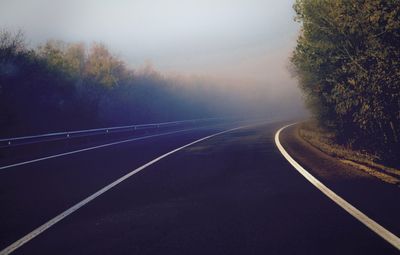 Road amidst trees against sky during foggy weather