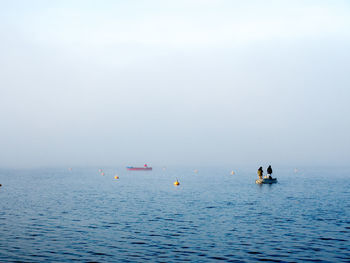 Two boats with three people fishing on foggy lake