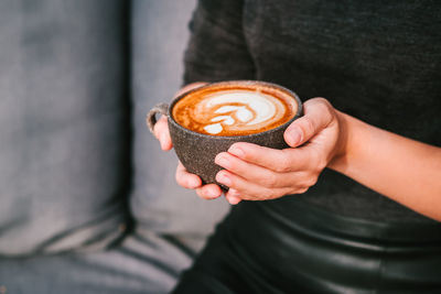 Woman in a black clothing holds coffee in a grey ceramic cup. latte art coffee cup.