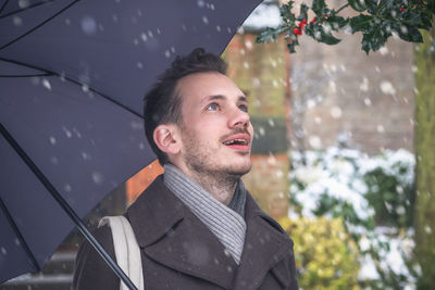 Happy mid adult man looking up in city during snowfall