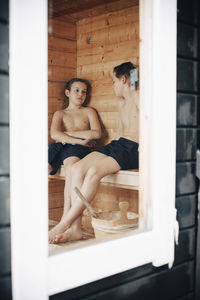 Shirtless boys talking in sauna seen through window