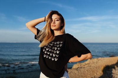 Young woman standing at beach against sky