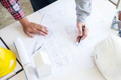 Cropped hands of architects drawing blueprint at desk