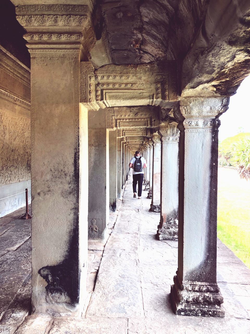 REAR VIEW OF MAN WALKING ON COLONNADE