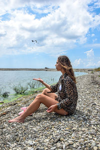 Woman sitting on pebbles at beach against sky