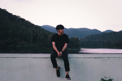 Full length portrait of young man sitting on wall