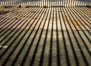 Shadow of railing on footpath during sunny day