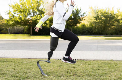 Side view of paralympic female runner with artificial leg doing exercises on lawn in urban park during active training
