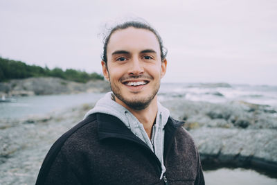 Portrait of young man standing at beach against sky
