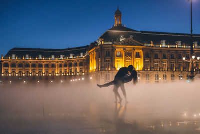 Full length of woman standing by illuminated building against sky at night