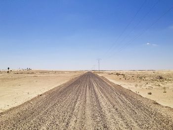 Road amidst desert land against clear blue sky