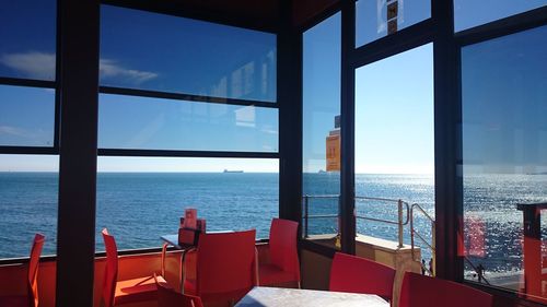 Chairs and table by sea against sky seen through window