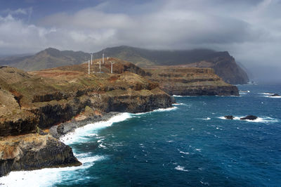 High angle view of rocky coastal feature against clouds