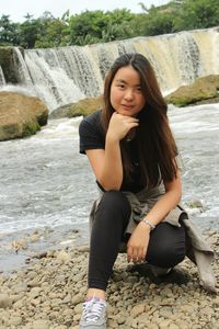 Young woman crouching against waterfall