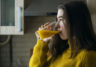 Teen girl drinks orange juice at home by the window