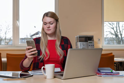 Businesswoman using mobile phone while sitting by laptop in office