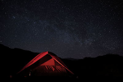 Tent and silhouette mountains against star field at night