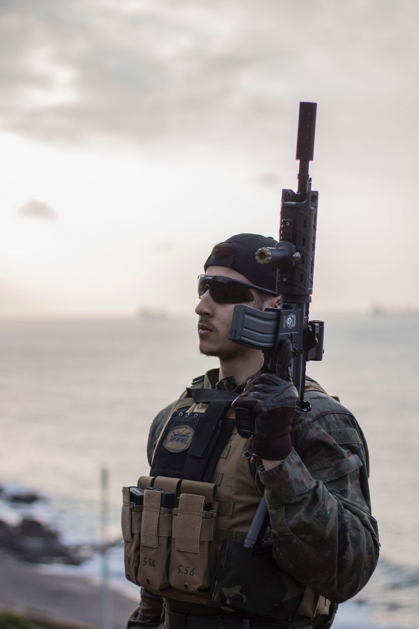 sea, one person, sky, standing, young adult, cloud - sky, men, war, beach, adults only, outdoors, headwear, adult, people, one man only, army, military, warrior - person, day, camouflage clothing