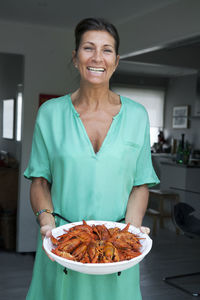 Smiling woman holding crayfish on plate, sweden