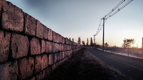 Retaining wall by empty road against sky during sunset