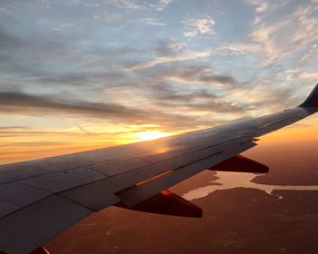 Airplane wing against sky during sunset