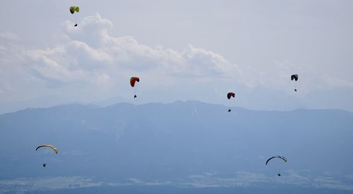 Low angle view of people paragliding against sky