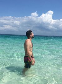 Side view of shirtless man standing in sea against sky