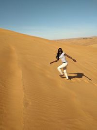 Woman on sand dune in desert against sky