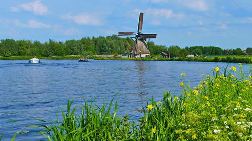 Traditional windmill by lake against sky