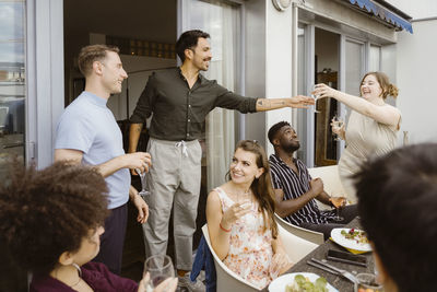 Smiling woman passing wineglass to male friend at dinner party in balcony